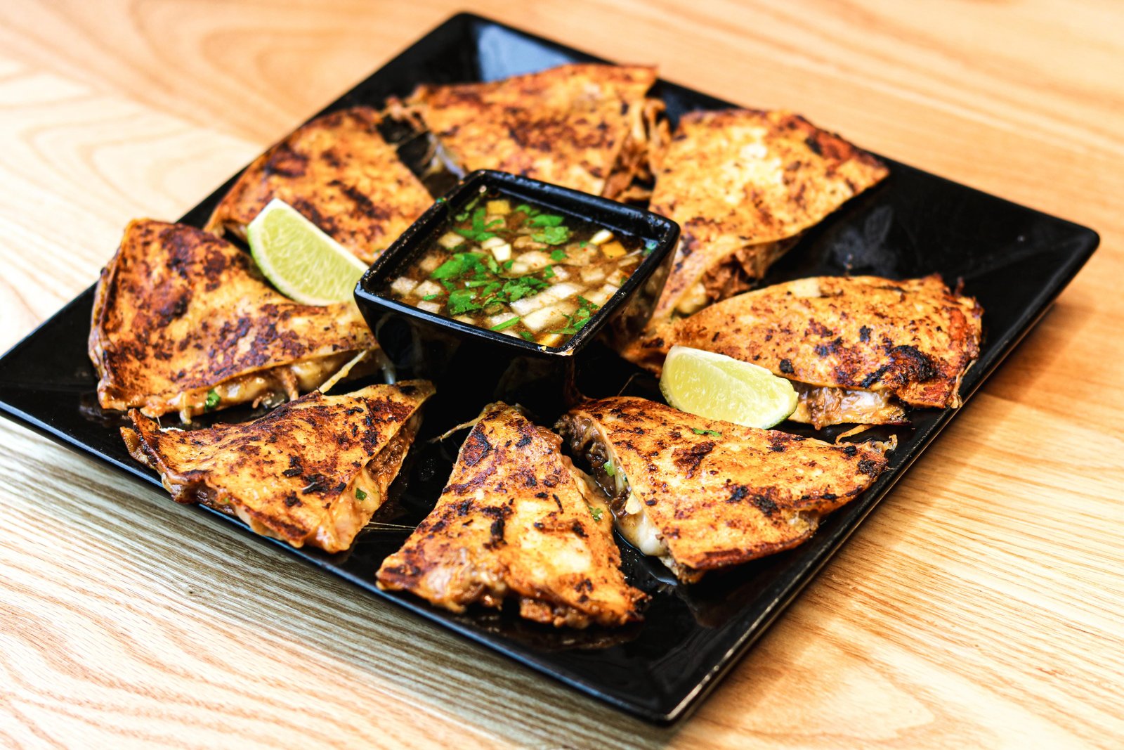 Birria-style pizza wedges with consommé for dipping and lime wedges, happy hour at Tequila Fuego Longview.