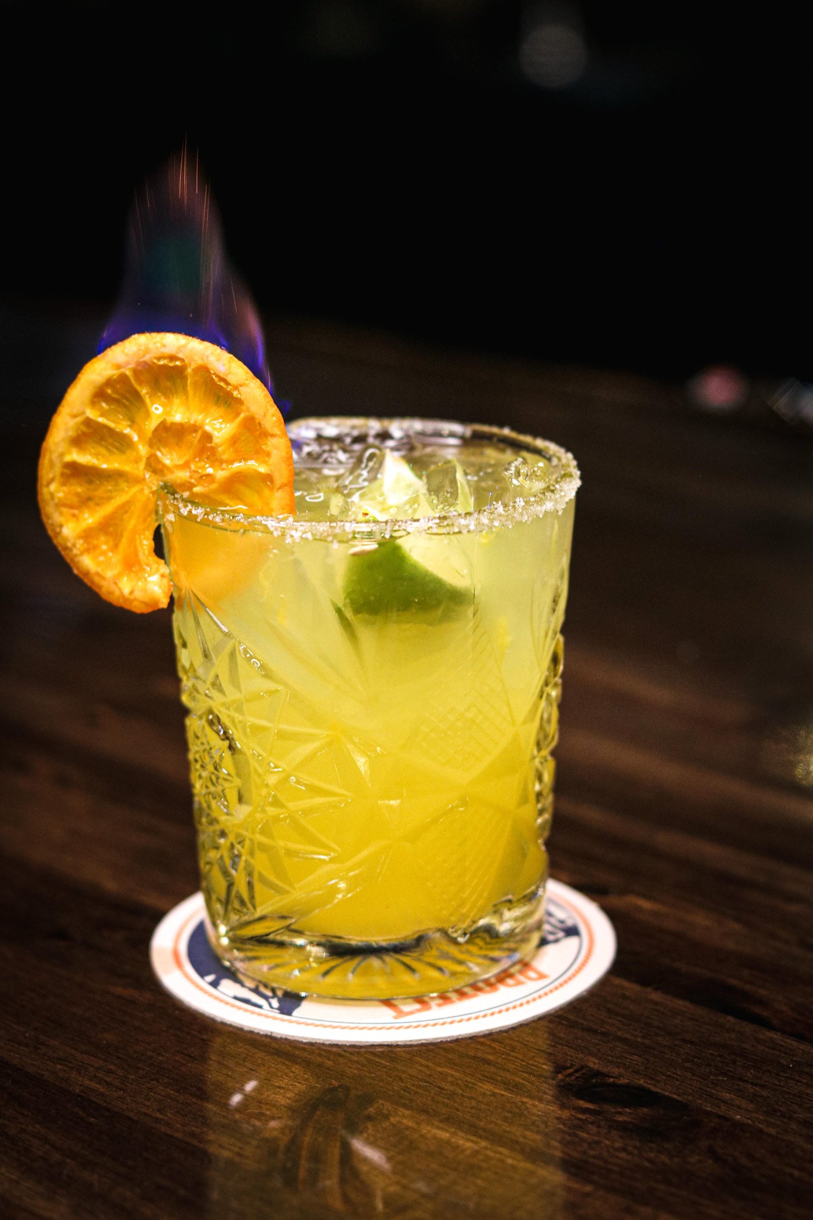 Paloma cocktail with tequila or mezcal, salted glass, lime, and flaming orange slice, happy hour Tequila Fuego Longview.